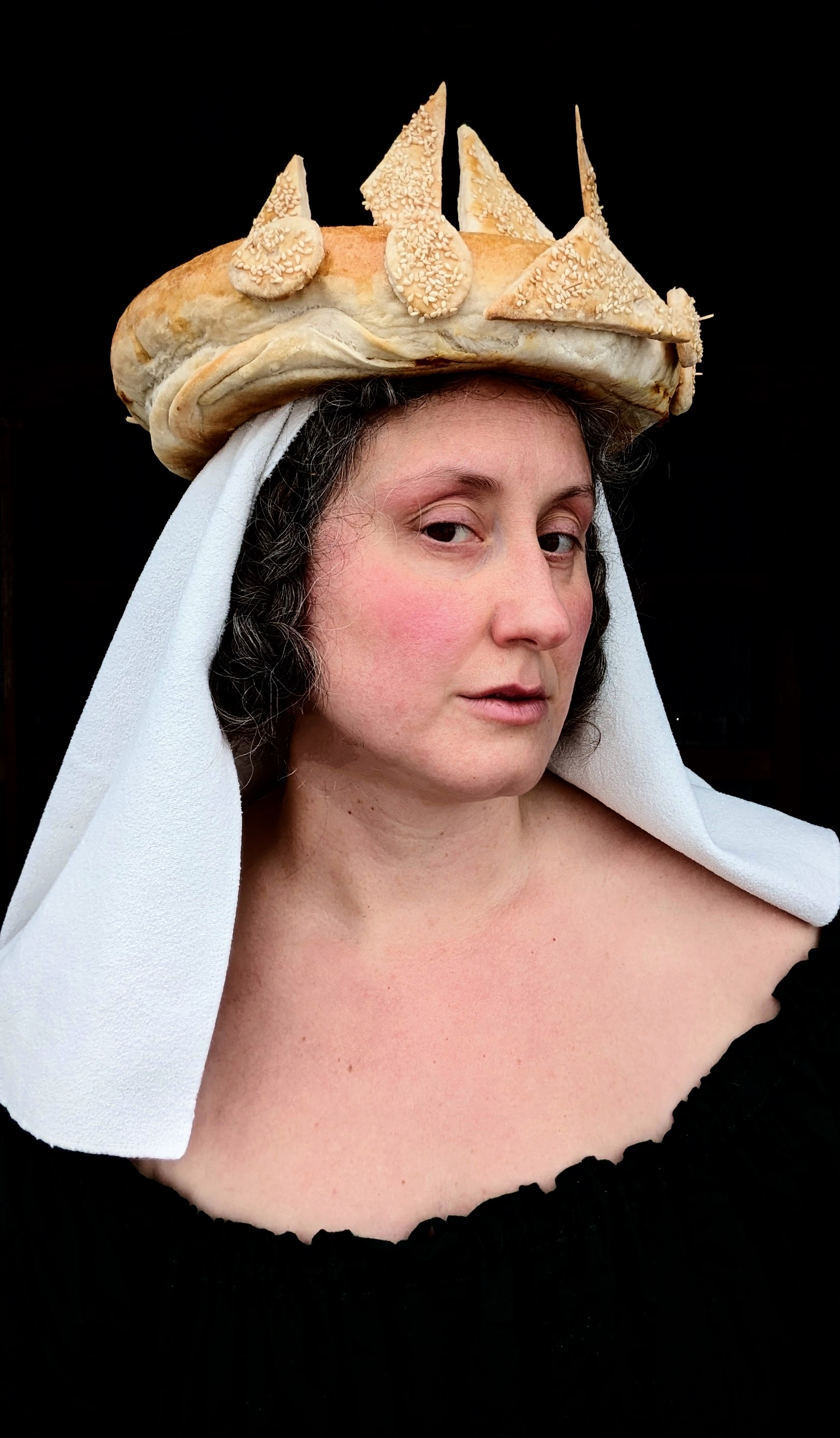 A woman wearing a wimple and crown of bread, posed like a medieval illustration.